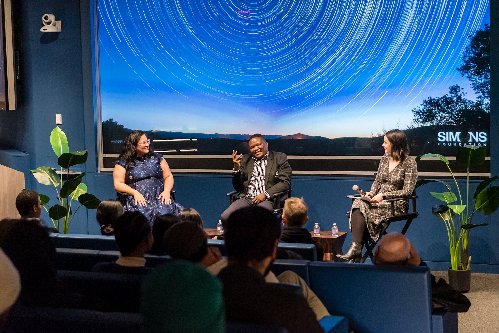 Three people sitting in director's chairs in front of an audience.