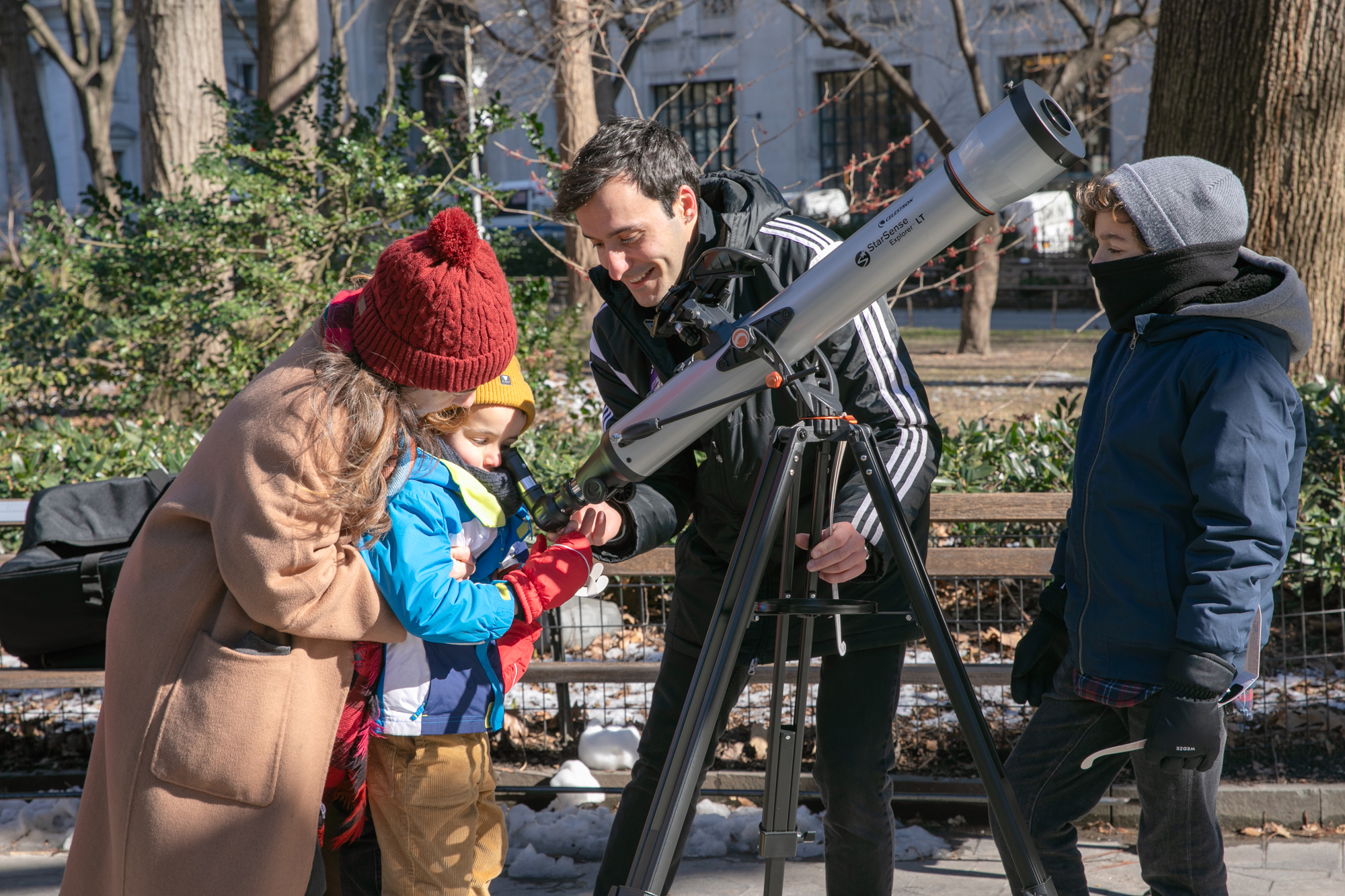 Three people looking through a telescope in a park
