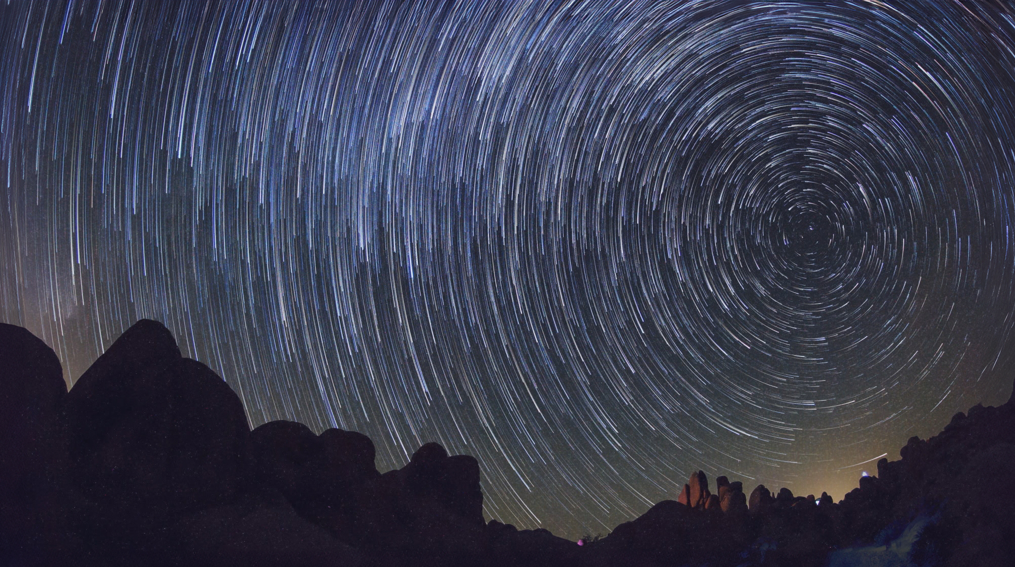 Slow exposure of night sky with stars swirling over a darkened landscape.