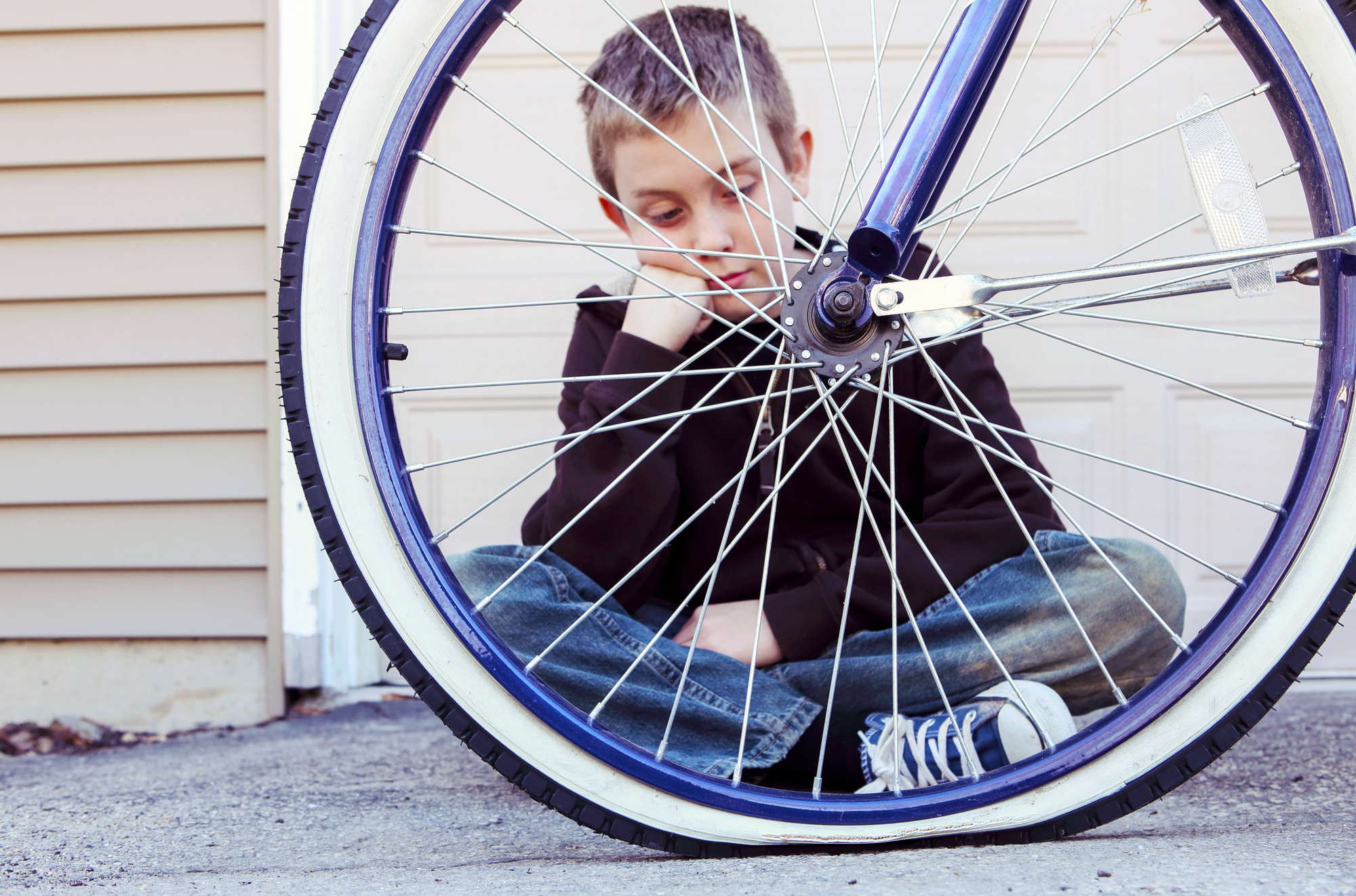 A photo of a boy looking at the one flat tire of the bicycle.