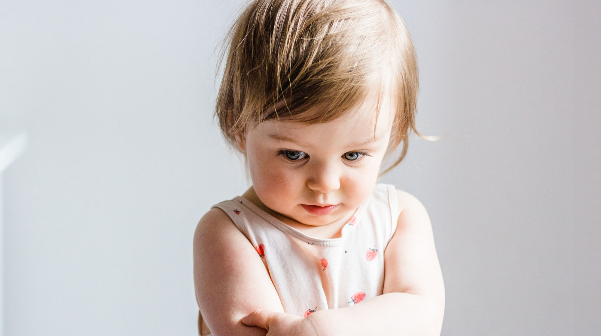 Sad or angry toddler baby girl looking down with her arms crossed.
