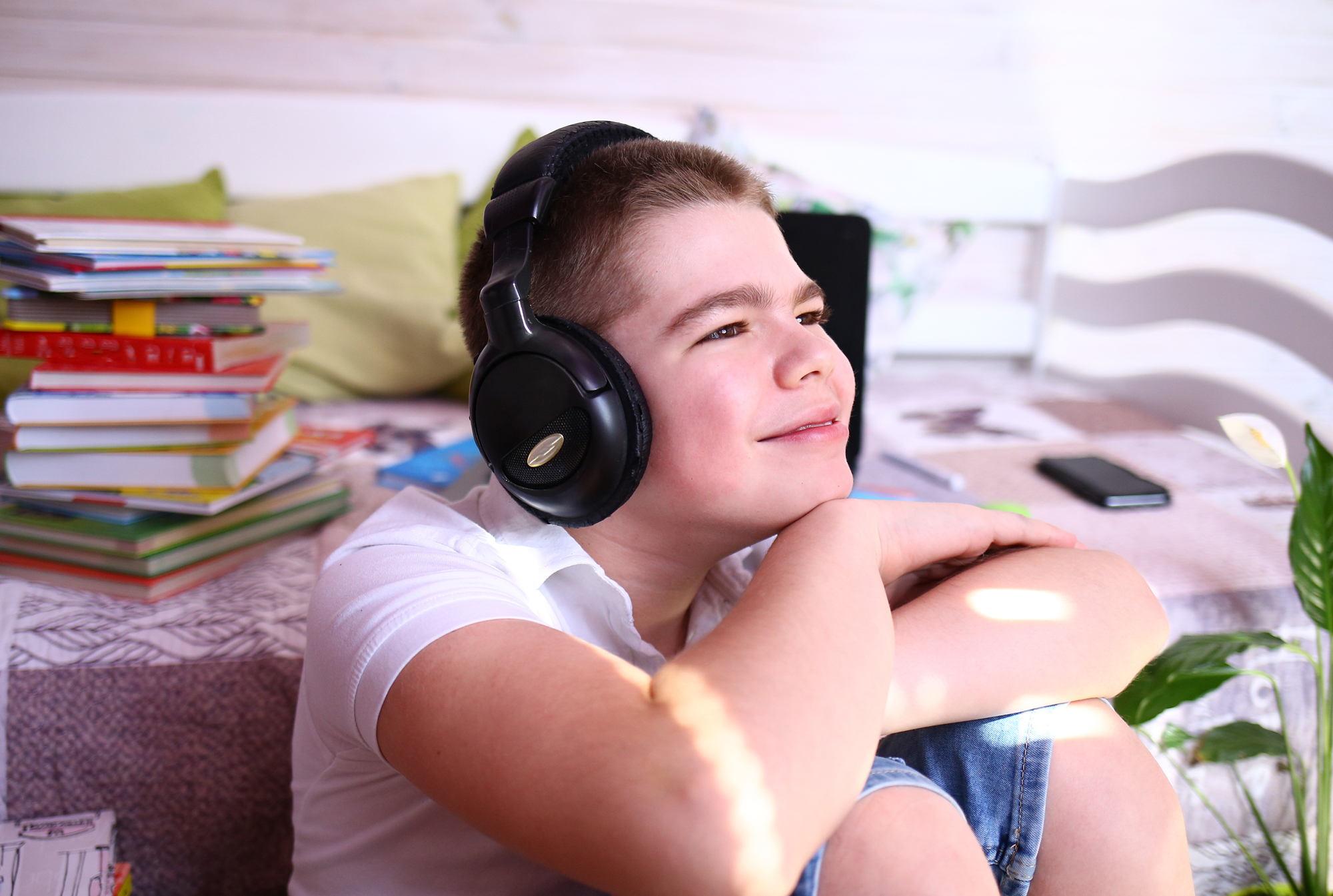 Portrait of smiling boy wearing headphones with books sitting on the table behind him.