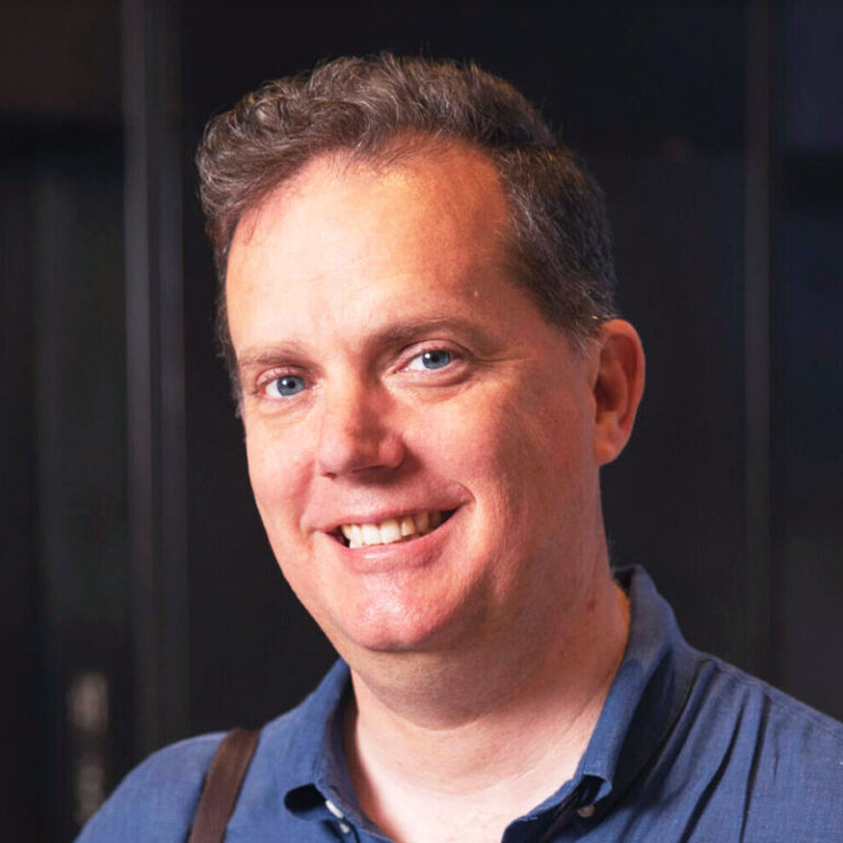 A smiling man in a blue collared shirt.