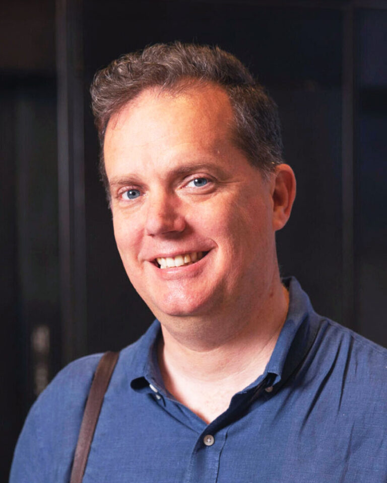 A smiling man in a blue collared shirt.
