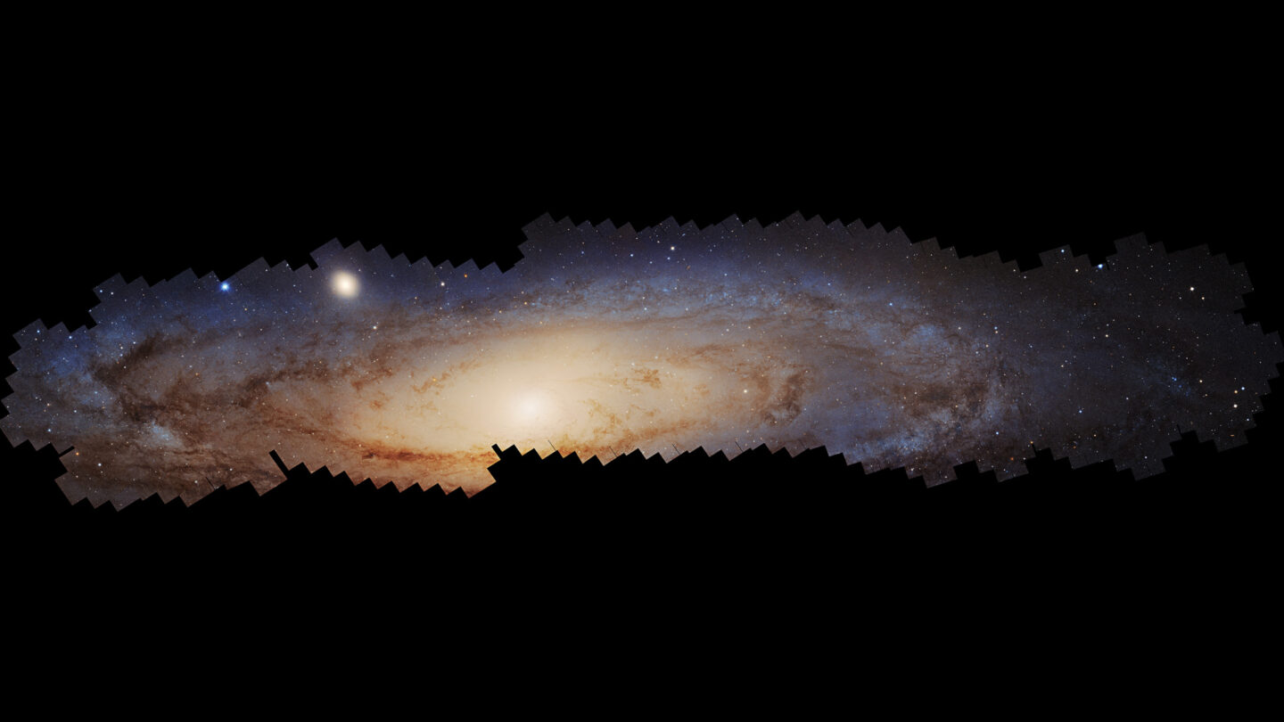 A wide, panoramic view of the Andromeda Galaxy featuring a bright central core surrounded by a spiral disk of stars and dust.