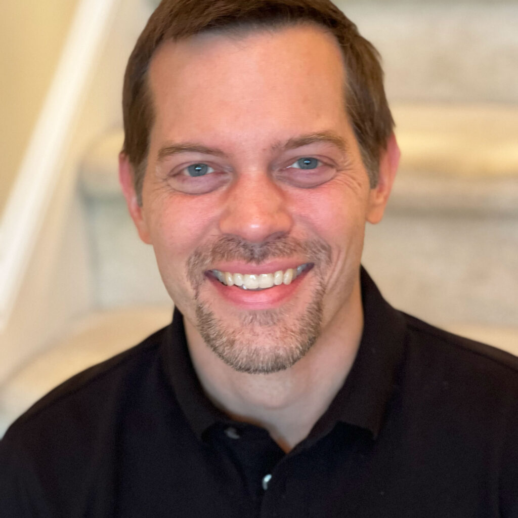 A man with short brown hair and a goatee smiling at the camera.