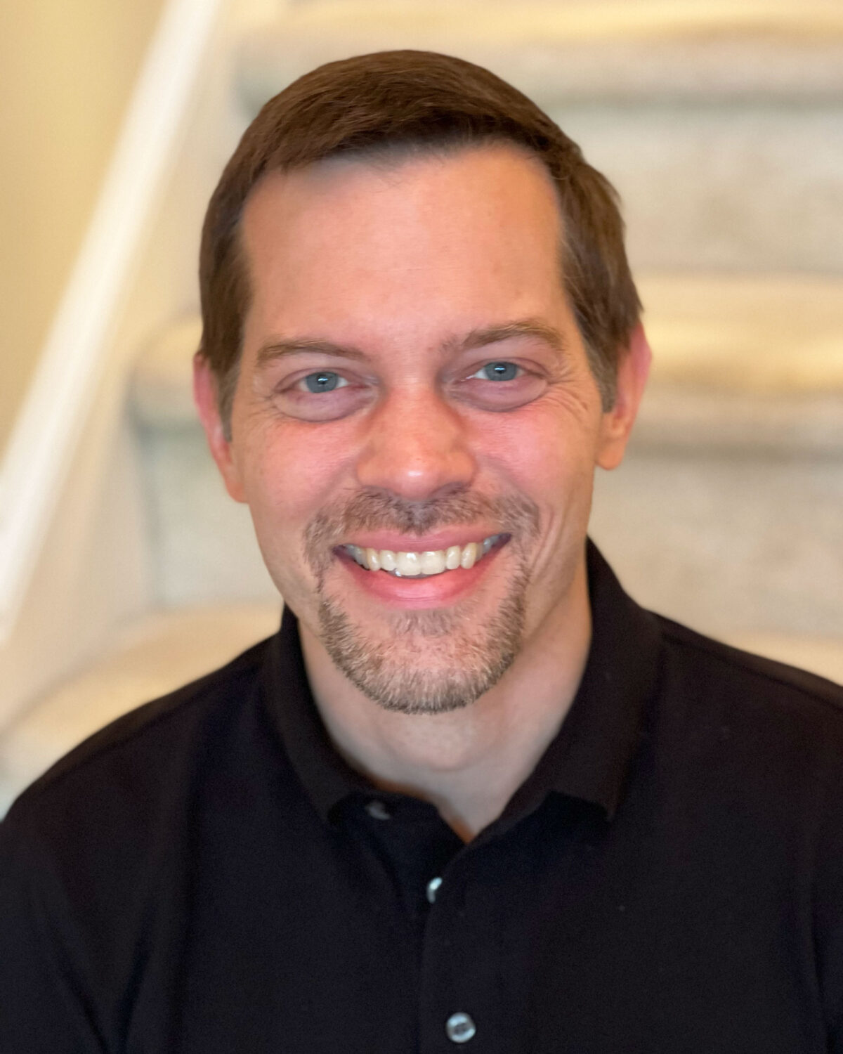 A man with short brown hair and a goatee smiling at the camera.