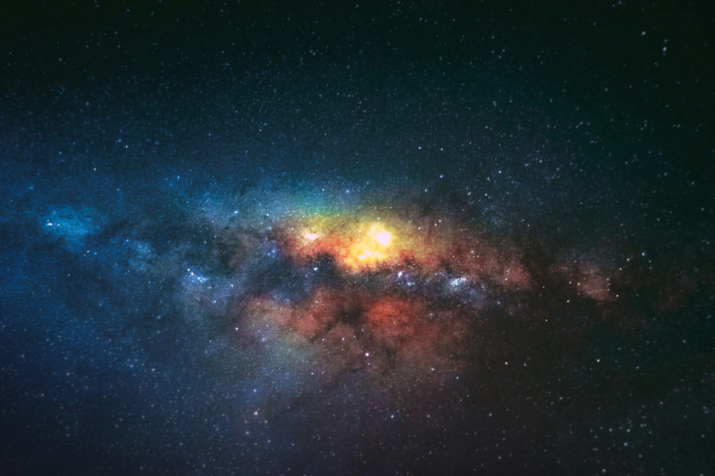 Bright, colorful section of the Milky Way galaxy with stars, glowing dust clouds, and nebulae against a dark night sky.