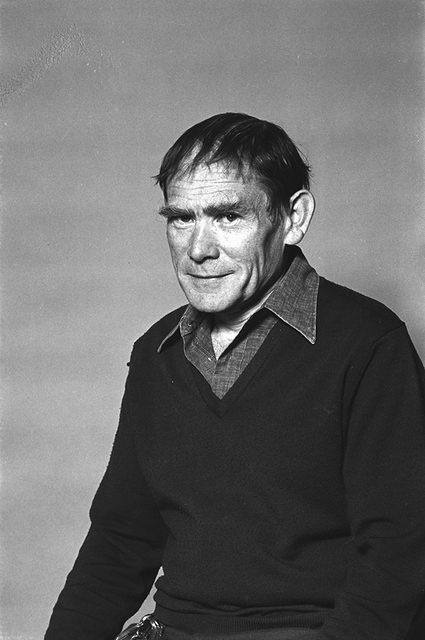 A middle-aged man with short, dark hair wearing a dark sweater over a collared shirt sits against a plain background, looking slightly to the side with a neutral expression.