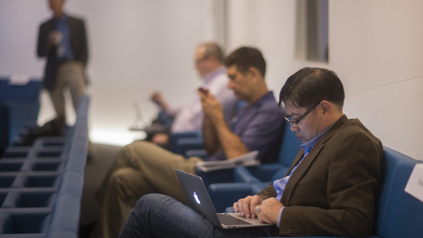 Three men in the back row of a lecture hall on their personal electronic devices