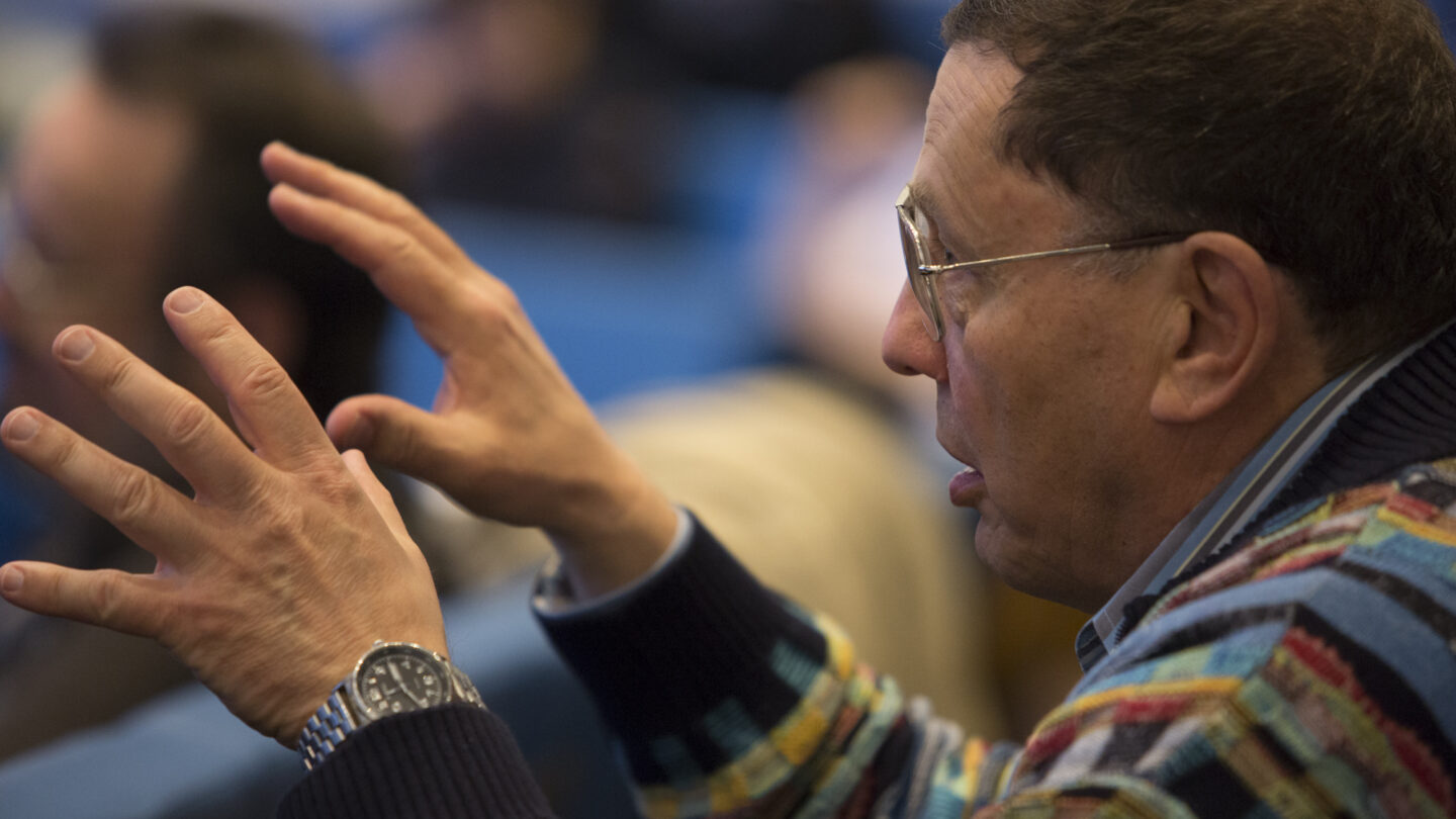 Man gesticulating with both hands as he sits in a lecture hall