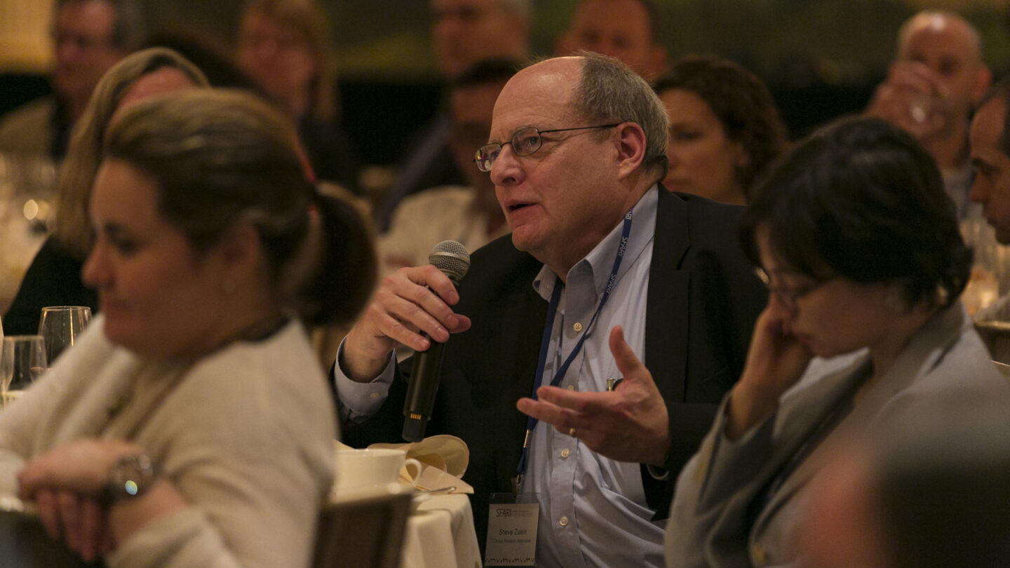 Man sitting at a table while talking into a microphone