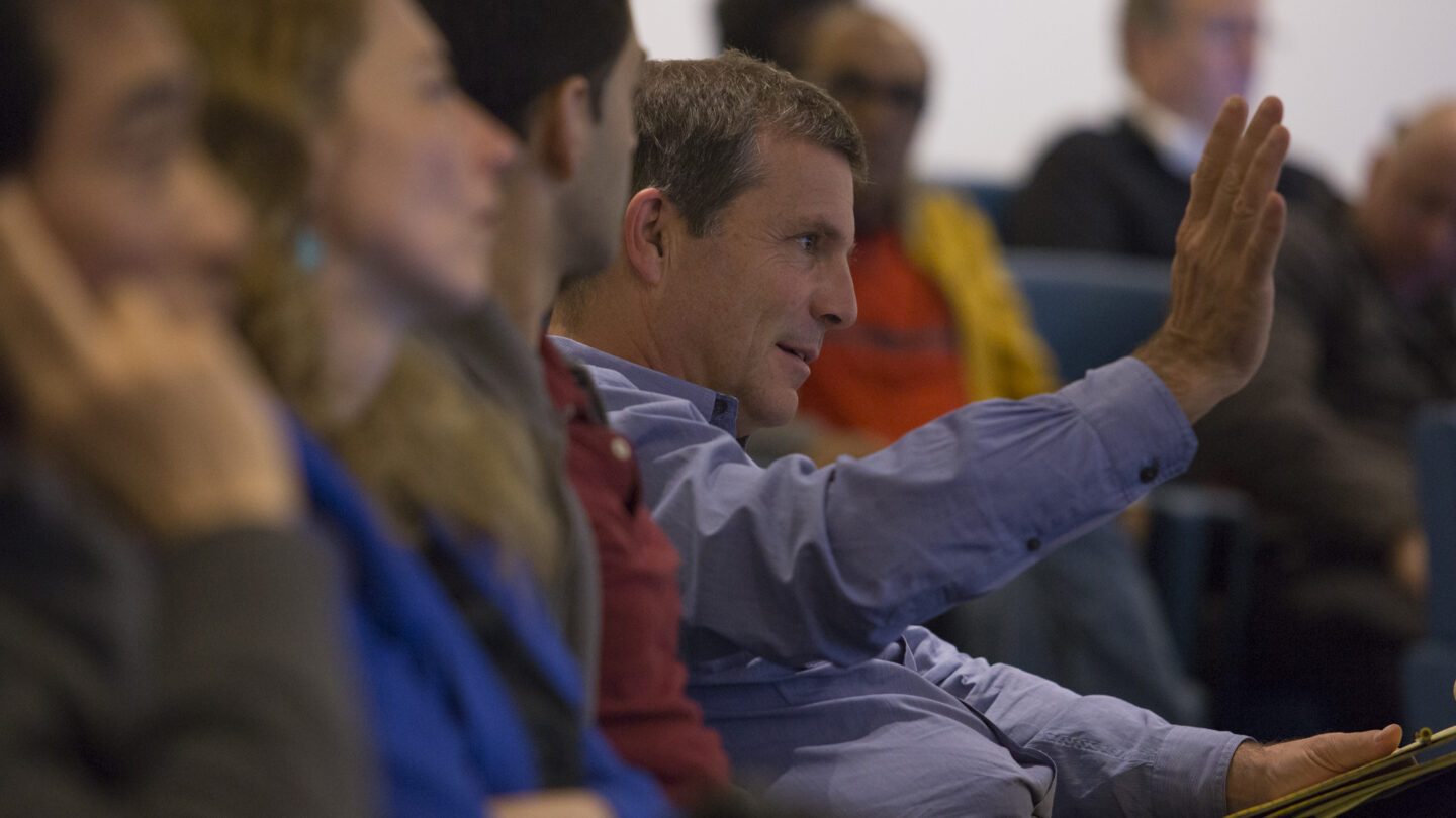 Man talking and gesticulating while sitting in lecture hall