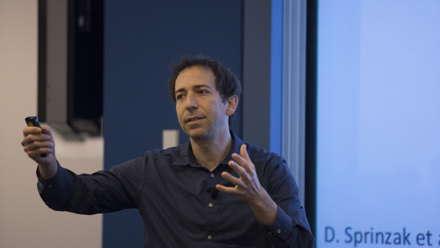 Man standing while talking, in front of a slideshow that says D. Sprinzak et al