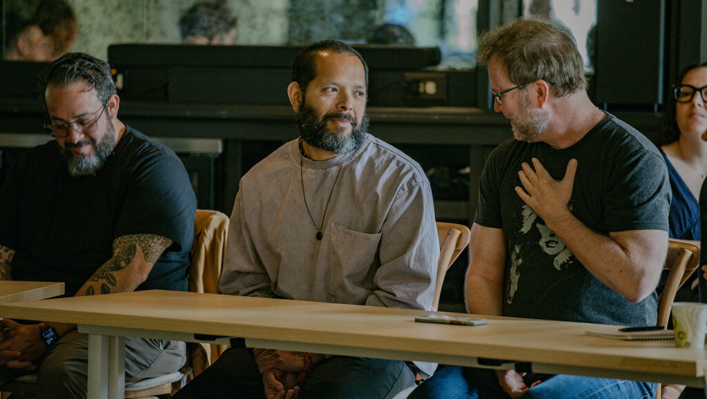 Three people seated at a wooden table smile and have a conversation