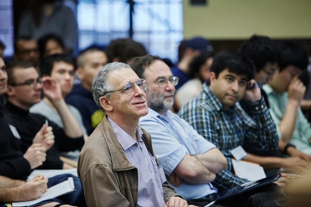 Man smiling in his seat amid a lecture hall full of people