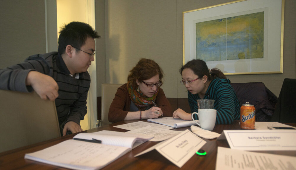 Bo-Xiao, Barbara and Qiaoni sitting at a table filled with papers while collaborating
