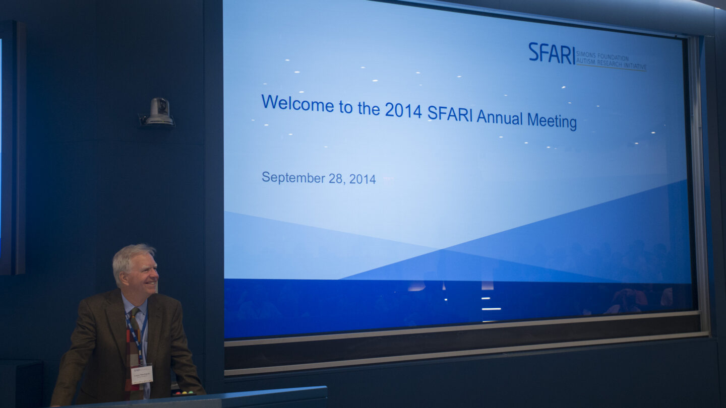 Man standing behind a lectern as he presents a slideshow that says 