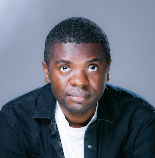 A man wearing a dark denim jacket over a white shirt looks upward slightly, set against a soft, blue-grey background.
