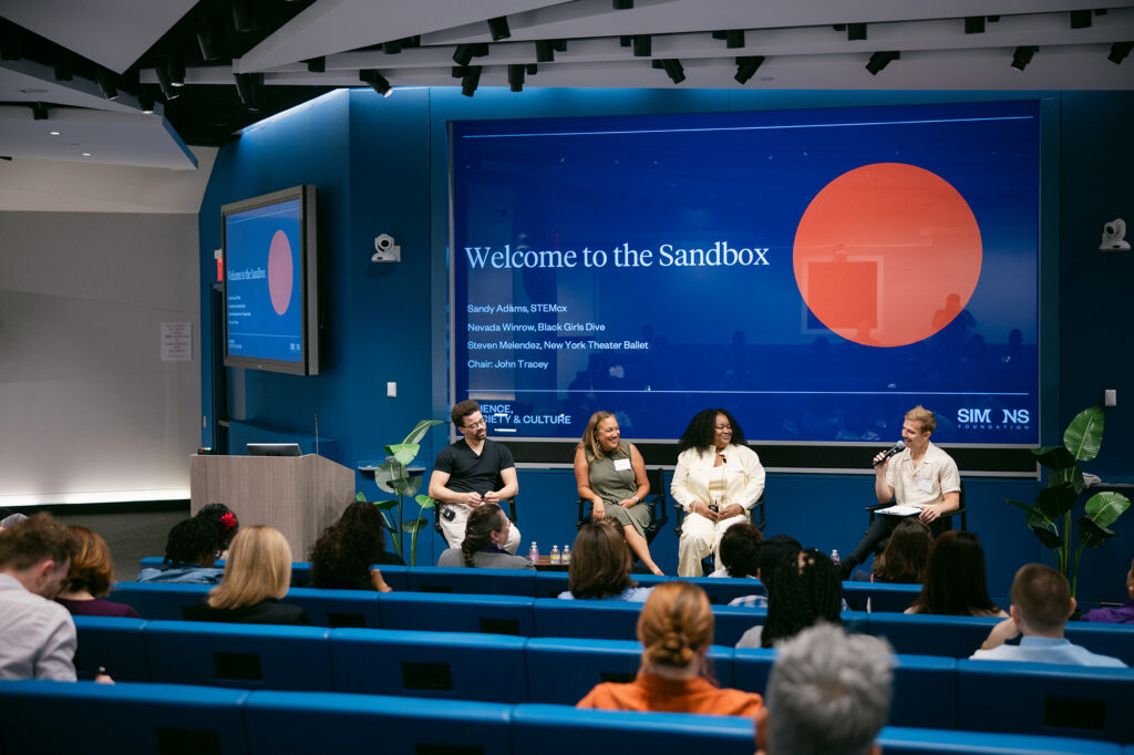 Panel of four speakers sitting in directors' chairs in an auditorium.