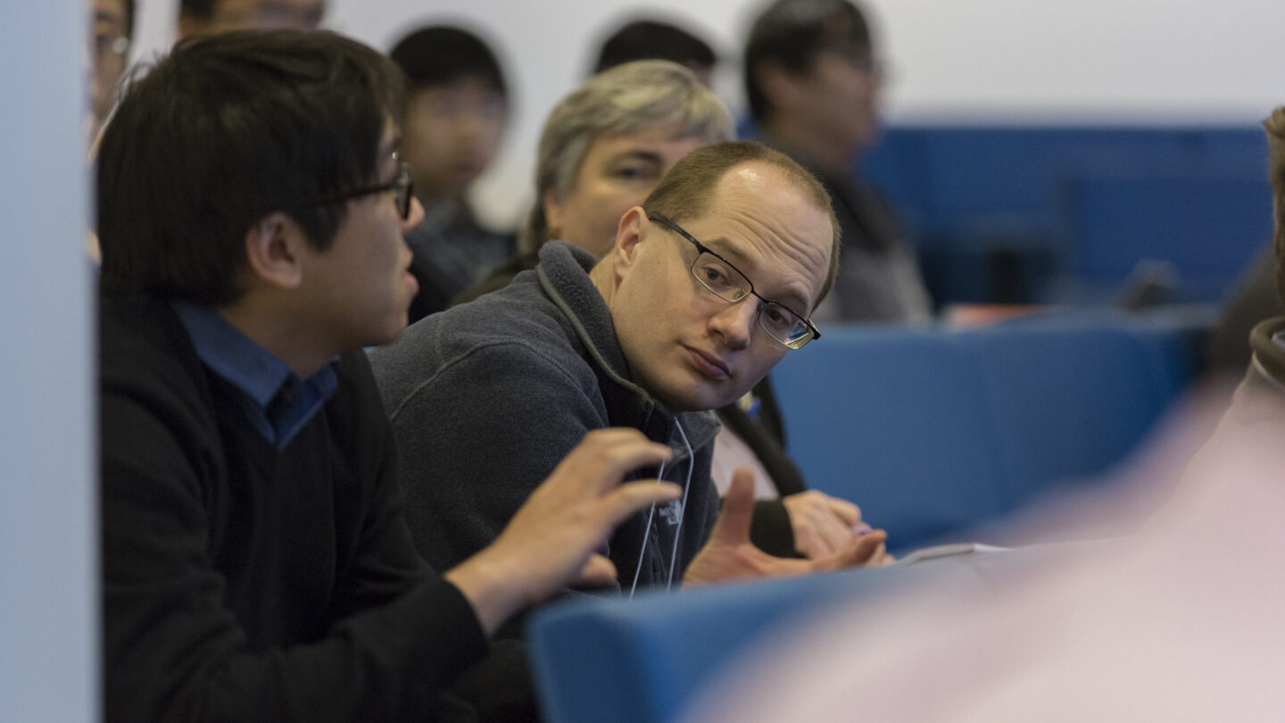 Man gesticulating as he sits in a lecture hall