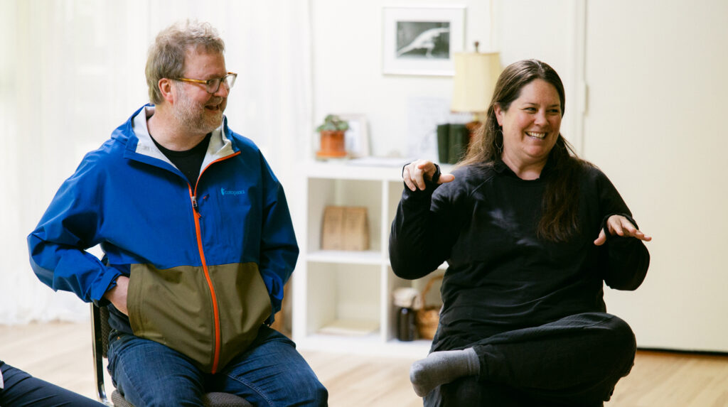 Two people smiling, seated in chairs.