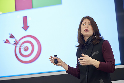 Woman standing with a clicker in hand in front of a slideshow