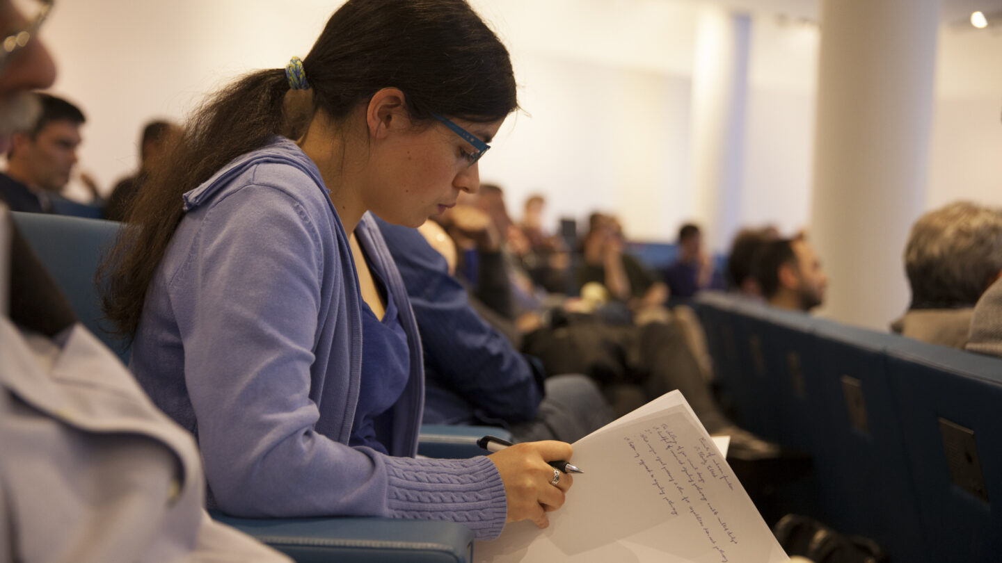 Woman sitting in a lecture hall while flipping a notebook page