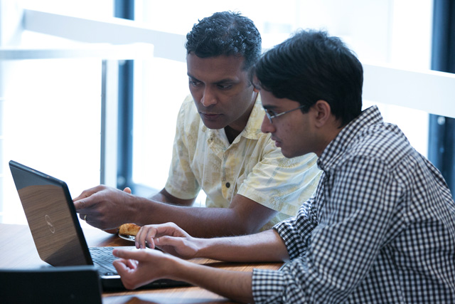 Two men sitting at a table together looking at a laptop