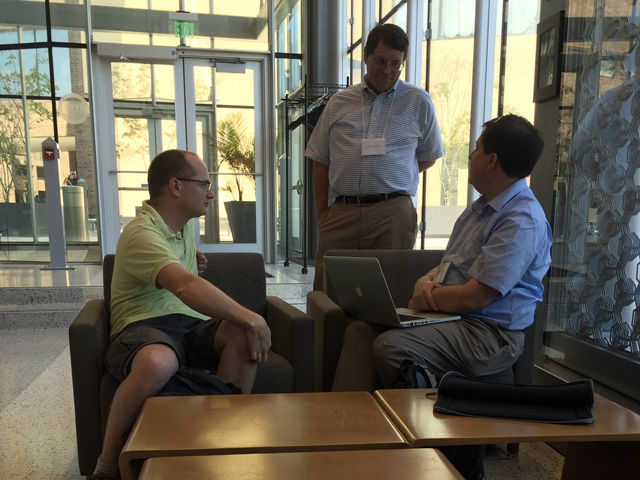 Two men sitting on individual couches, talking to one man standing