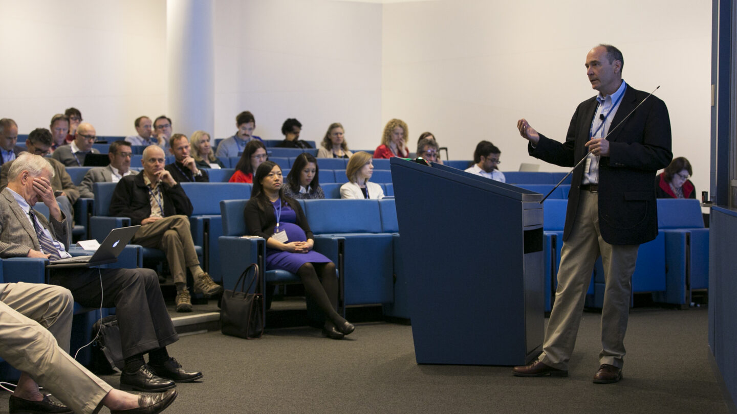 Man standing in front of a half-full lecture hall and talking