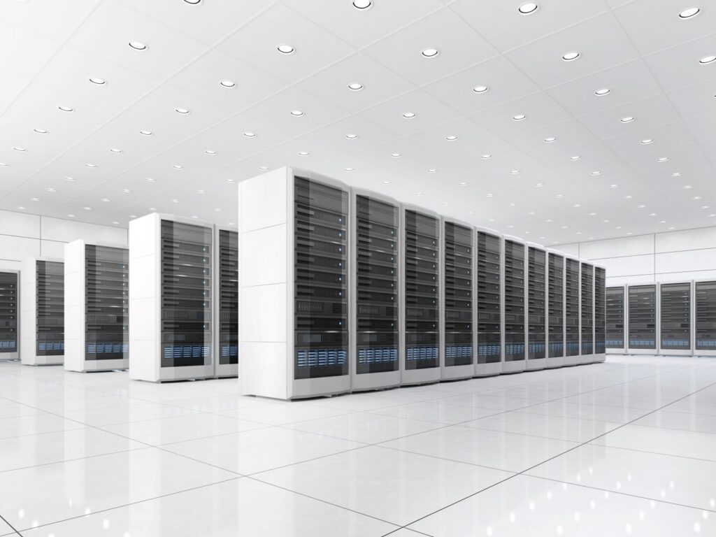 A photograph of computer servers in a white room. There are 5 rows of the servers coming from left to right, and at least one row of servers lined up against the wall of the room seen in the background.