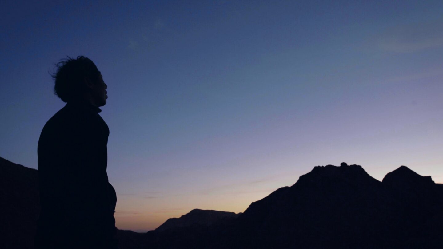 Silhouette of man's hair blowing, against sunset in the background