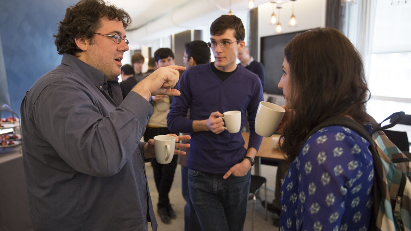 Three standing people holding mugs while talking