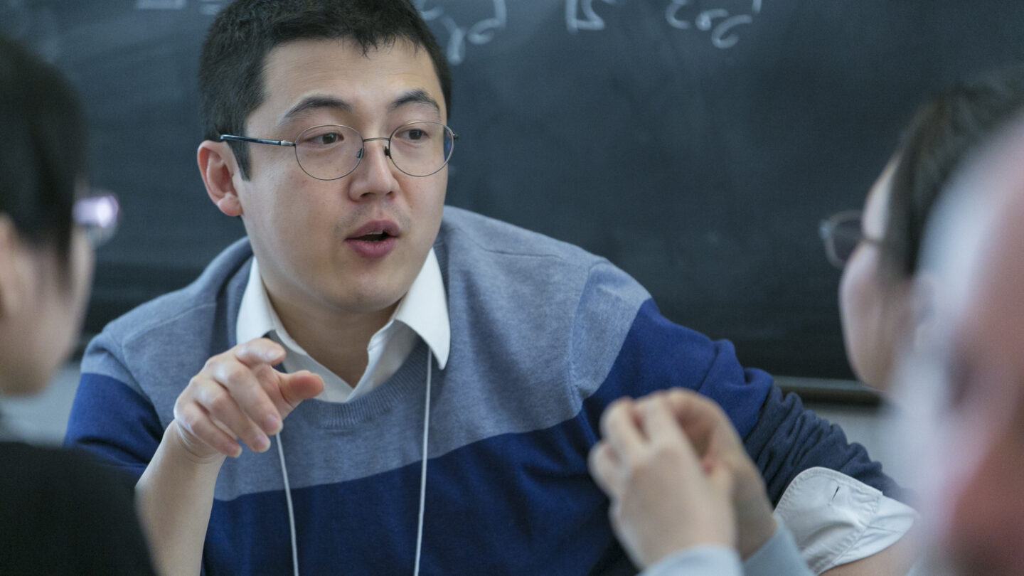 Man sitting at a table and talking as he points with his right hand
