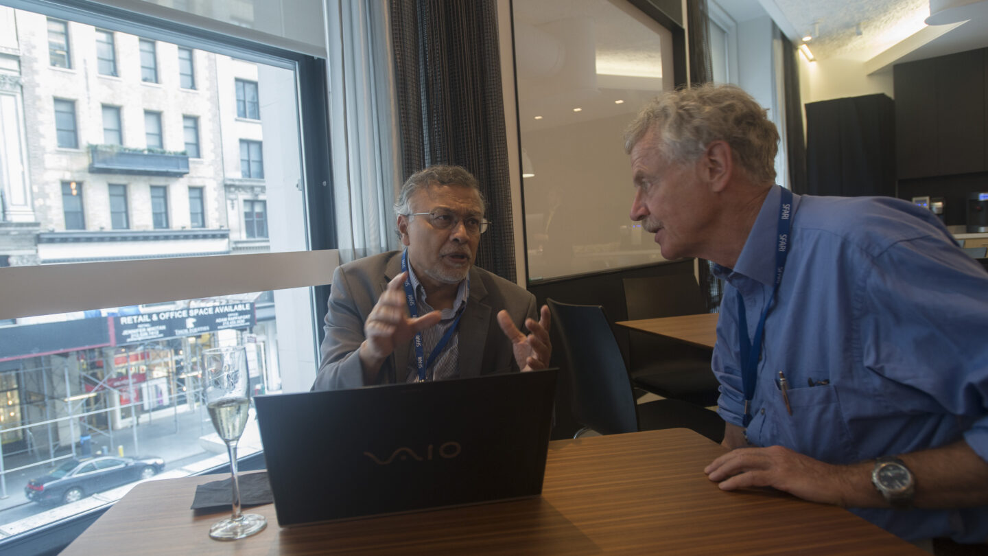 Two men at a table together with a computer