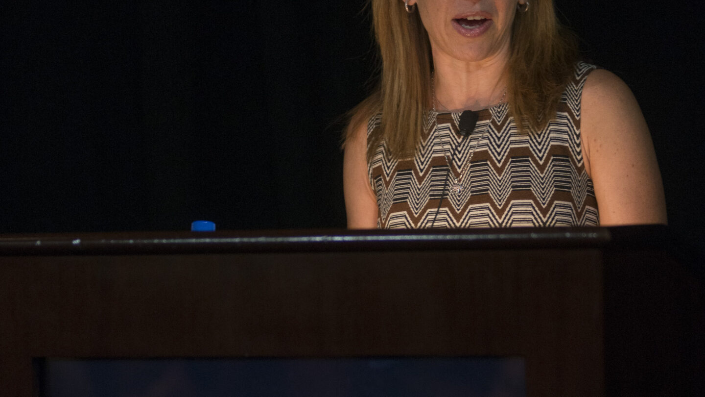 Woman standing behind a lectern that says SFARI Simons Foundation Autism Research Initiative