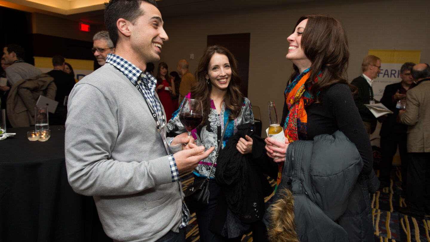 Three people standing and smiling as they hold alcoholic beverages