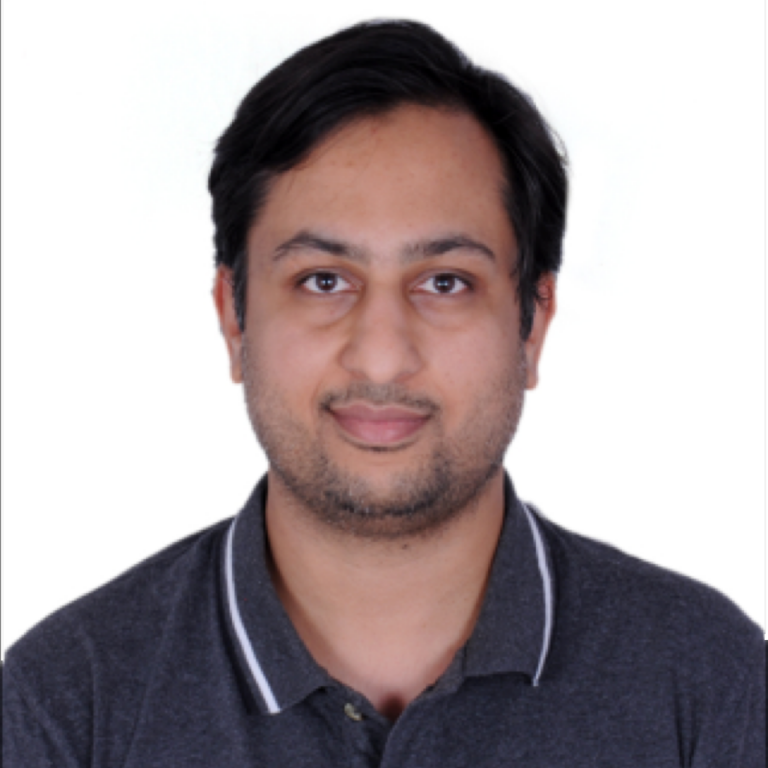 A man with short dark hair and a trimmed beard is facing the camera and smiling slightly. He is wearing a dark grey polo shirt with white trim. The background is plain white.