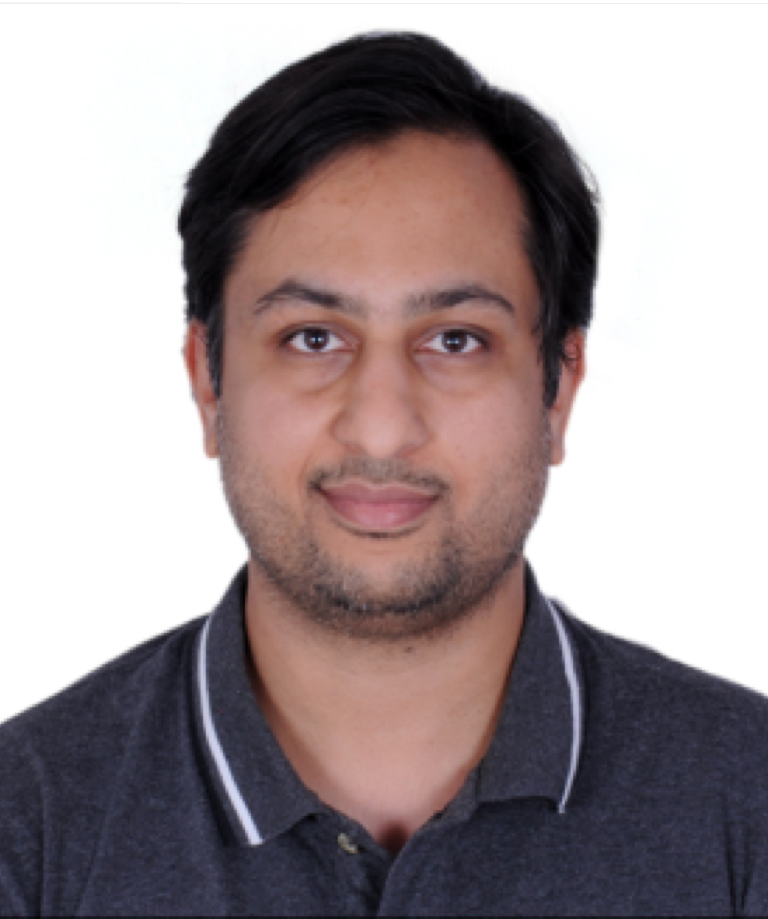 A man with short dark hair and a trimmed beard is facing the camera and smiling slightly. He is wearing a dark grey polo shirt with white trim. The background is plain white.