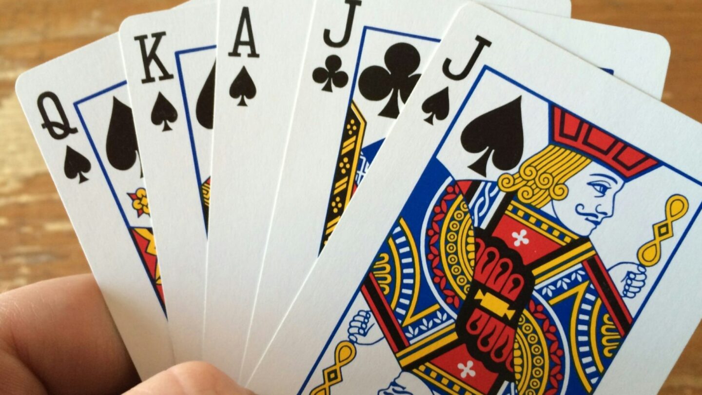 Hand holding queen of spades, king of spades, ace of spades, jack of clubs and jack of spades cards