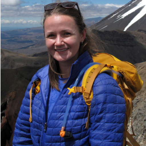 Clair Nichols carrying a yellow hiking backpack as she stands on top of a high elevation rock