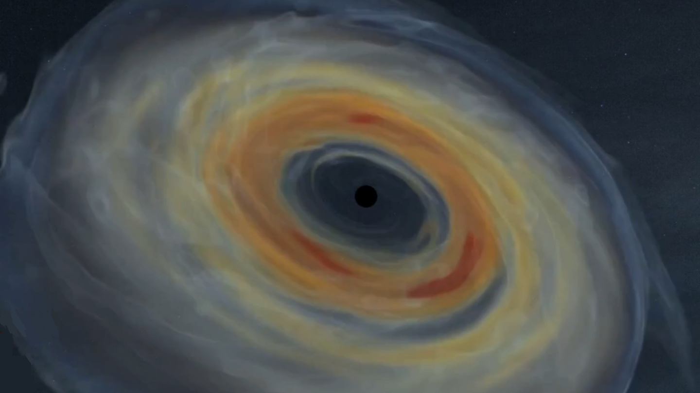 A swirling accretion disk of bright yellow, orange, and gray gas encircles a dark central black hole against a star-speckled background in space.
