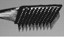 Close-up of a black rectangular microelectrode array with many fine, needle-like projections extending downward, mounted on a bundle of wires against a gray background.