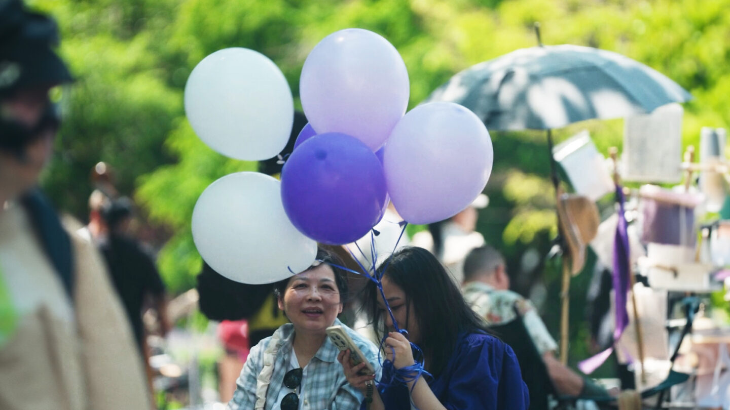 Girl holding balloons and phone standing next to her mom.