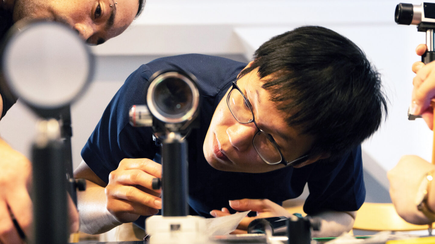 A photo of a student looking into a benchtop microscope.