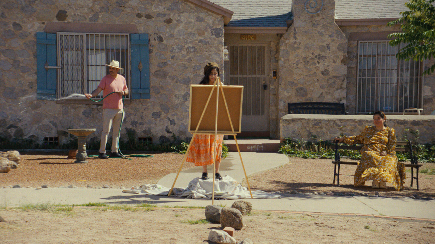 Person standing in front of window; person standing at an easel; woman sitting on a bench