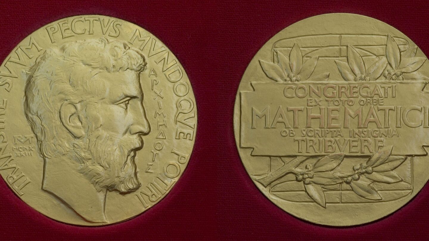 Two gold medals featuring engravings; the front shows a bearded mans profile with Latin text, and the back displays a rectangular panel with more Latin text and laurel branches, set against a dark red background.
