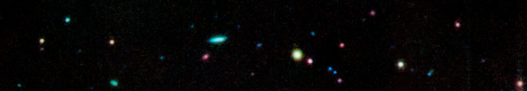 A field of stars and galaxies in deep space, showing colorful points of blue, red, and yellow light scattered across a dark background.
