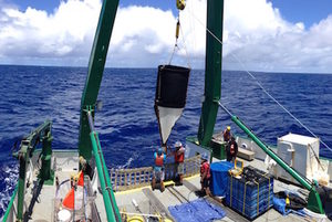 Researchers on a ship deploy oceanographic equipment into the deep blue sea under a partly cloudy sky, using a large green crane.